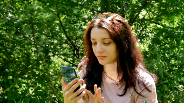 Erstaunliche-Mädchen-lacht-lesen-Nachricht-im-sozialen-Netzwerk-auf-ihrem-Handy.-Closeup-Portrait-schöne-Brünette-Frau-mit-blauen-Smartphone-im-Freien-auf-grüne-Bäume-Hintergrund.