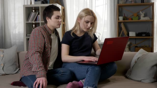 Zwei-junge-lesbische-Mädchen-auf-der-Couch-sitzen,-mit-Hilfe-eines-Computers,-Scrollen-im-Internet,-Einkaufen-online-60-fps