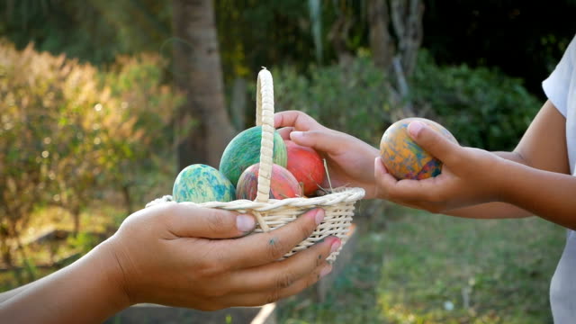 Primer-plano-de-mano-de-mujer-sosteniendo-una-cesta-con-huevos-de-Pascua-y-su-dando-a-los-niños-en-el-fondo-de-la-luz-del-sol
