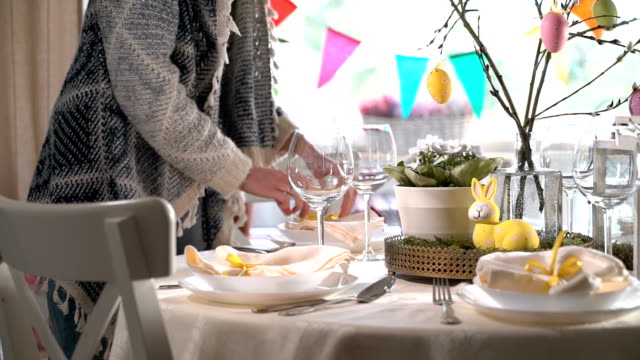 Young-woman-setting-easter-festive-table-with-bunny-and-eggs-decoration