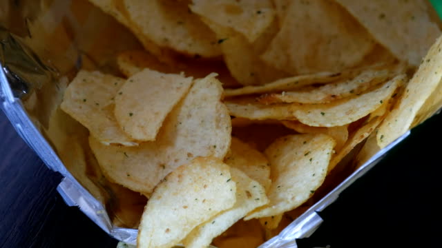 Kartoffel-Chips-im-Paket-auf-den-Tisch.-Weibliche-Hand-nimmt-chips