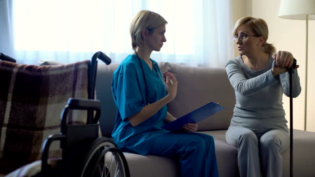 Female-doctor-talking-to-senior-woman-at-hospital,-making-notes,-rehabilitation