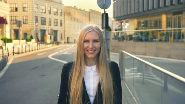 Formal-business-woman-walking-on-street.-Elegant-blond-woman-in-suit-standing-on-street-with-smile-against-urban-background