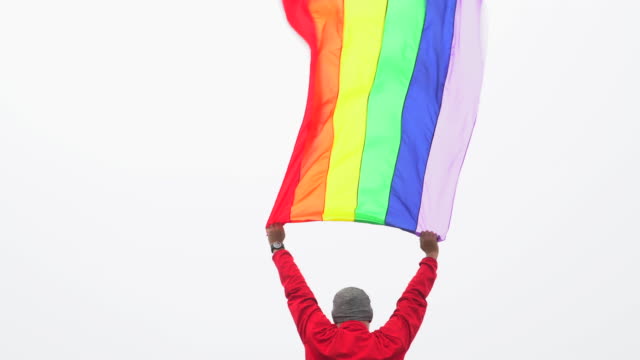 hombre-levantar-bandera-LGBTI-de-color-arco-iris-ondeando-en-duro-viento-en-el-mirador-de-alta-montaña