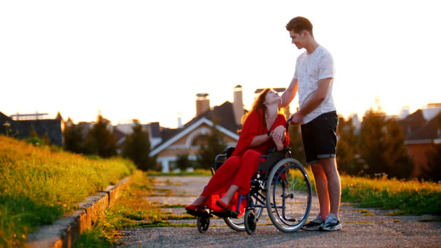 Mädchen-In-einem-netten-Gespräch-mit-ihrem-jungen-Mann-auf-dem-Hintergrund-des-Hauses,-grünen-Rasen-und-Bäumen-Rollstuhl