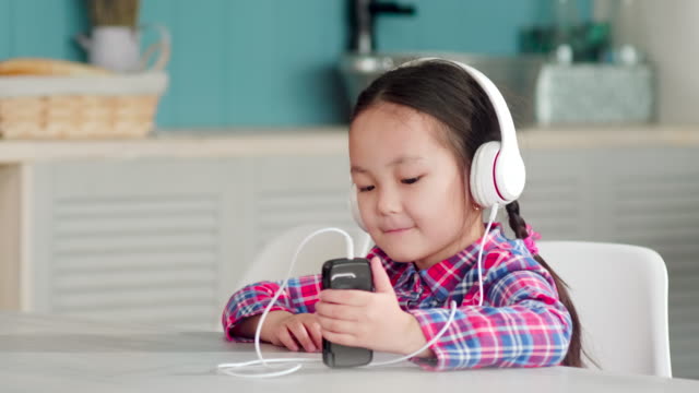 Little-Asian-Girl-in-Headphones-Listening-to-Music-on-Smartphone