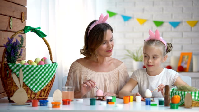 Little-daughter-kissing-mother-on-cheek-helping-with-Easter-eggs-decor,-love