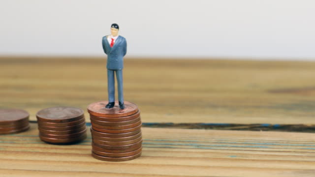 Miniature-people-standing-on-piles-of-coins