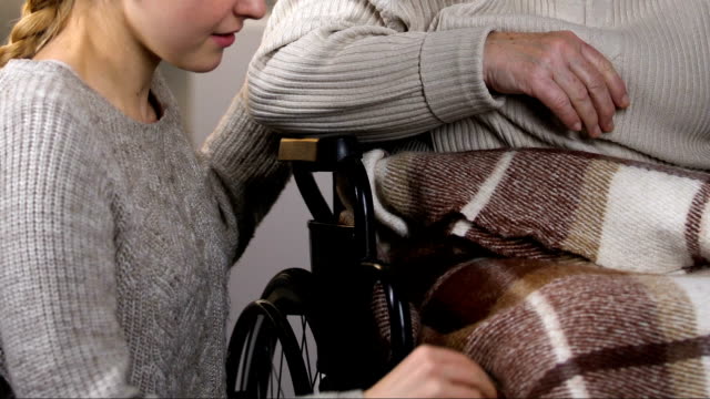 Aufmerksame-junge-Dame-Verkleidung-deaktiviert-Oma-im-Rollstuhl-mit-Karomuster,-umarmen