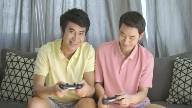 Pareja-gay-asiático-joven-competitivo-empuja-y-empujar-unos-a-otros-mientras-juegan-un-juego-de-video-en-casa