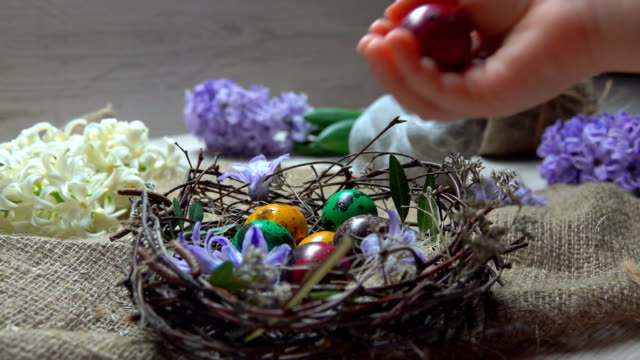 Child's-hand-lays-colored-egg-in-in-the-Easter-nest