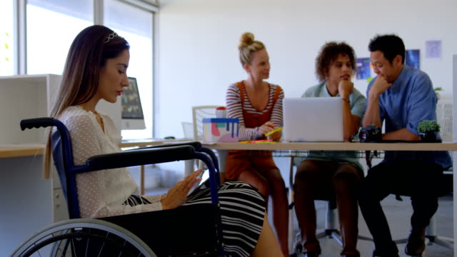 Seitenansicht-junger-kaukasischer-Behinderter,-die-an-einem-digitalen-Tablet-gegen-drei-Geschäftsleute-arbeiten