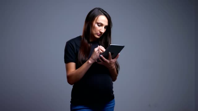 Closeup-portrait-of-pregnant-young-caucasian-woman-typing-on-the-tablet-looking-at-camera-and-smiling