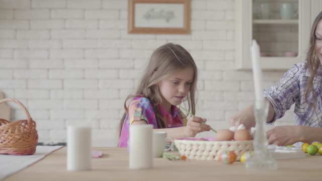 Cute-little-smiling-girl-painting-Eastern-eggs-with-a-small-brush-with-her-mom
