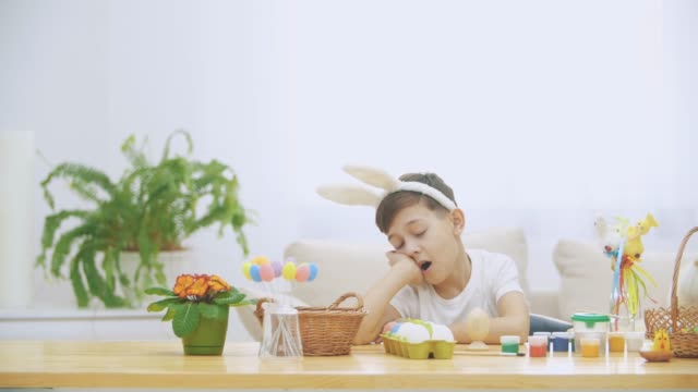 Cute-nice-boy-is-sitting-at-the-table,-but-got-tired-and-decided-to-have-a-rest.-Boy-is-yawning.-At-the-end-he-notices-interesting-bunnies-and-plays-with-them.-Playful-boy.