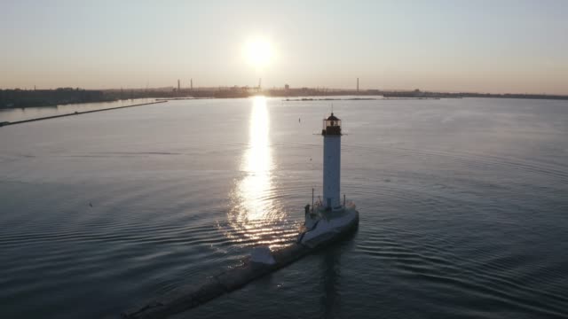 Aerial-shot-of-white-lighthouse-near-sea-port-during-sunset,-silhouette