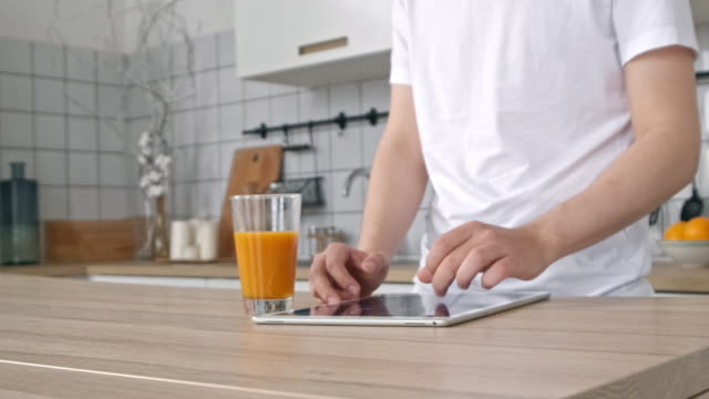 Attraktiver-Mann-zu-Hause-mit-Tablet-in-der-Küche-senden-Botschaft-auf-Social-Media-Lächeln-genießen-modernen-Lebensstil-trägt-weißes-Hemd