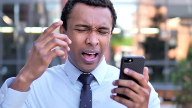 Hombre-de-negocios-africano-al-aire-libre-molesto-por-pérdida-mientras-usa-smartphone