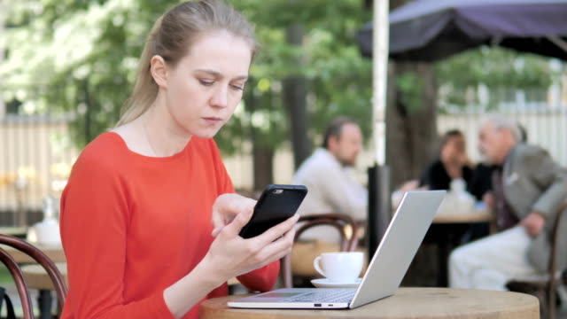 Junge-Frau-nutzt-Smartphone-und-Laptop-Sitting-in-Café-Terrasse