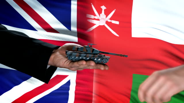 Gran-Bretaña-y-Omán-oficiales-intercambiando-tanque-por-dinero,-bandera-ejército-de-fondo