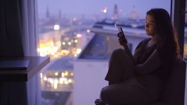 Close-up-woman-using-phone-on-windowsill-at-twilight