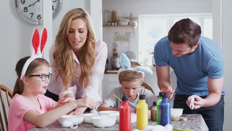 Family-sitting-around-kitchen-table-with-parents-helping-children-to-paint-eggs-for-Easter---shot-in-slow-motion