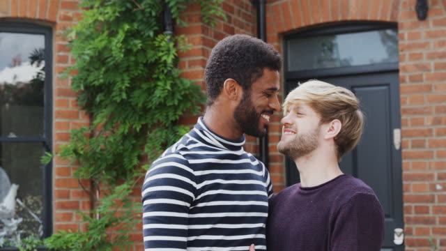 Retrato-de-pareja-gay-masculino-de-pie-fuera-de-un-nuevo-hogar-en-el-día-de-mudanza-juntos-besándose