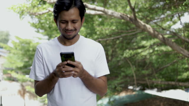 Junger-asiatischer-Mann-zu-Fuß-und-genießen-Smartphone-im-Freien