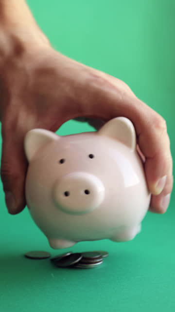 Mann-schütteln-Sparschwein-und-Münzen-fallen-auf-grünem-Hintergrund,-vertikale-video