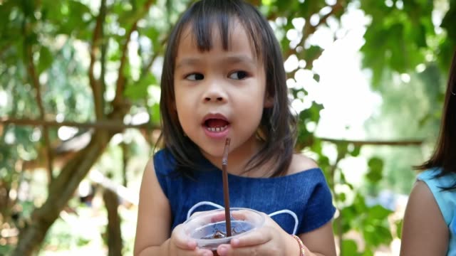 Little-Asian-child-girl-sipping-her-drink-while-sitting-rest-in-the-park-on-summer-day.-Selective-focus.