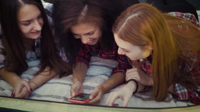 Fröhliche-Mädchen-entspannen-auf-Decke-und-mit-Smartphone-für-Spaß