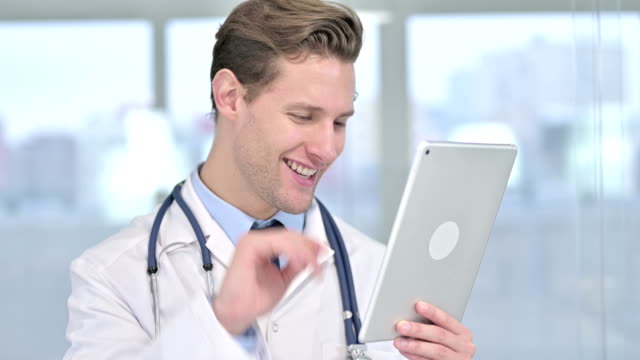Retrato-de-joven-hombre-alegre-Doctor-haciendo-video-chat-en-la-tableta