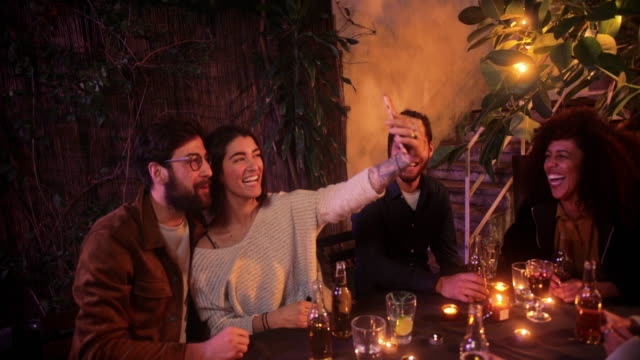 Kaukasisches-Paar-macht-Selfie-mit-Smartphone-während-Freunde-Terrasse-Party