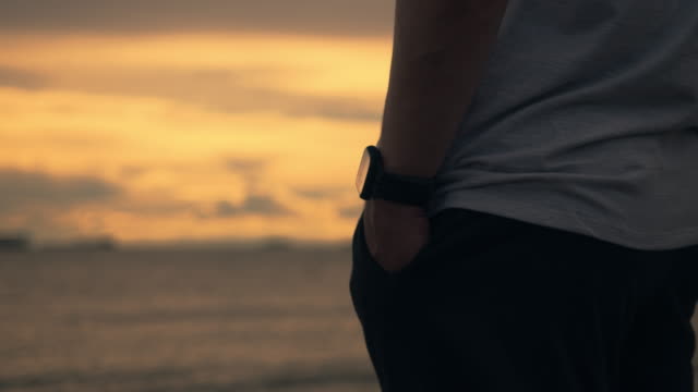 Nah-aufnahme-stattlich-Mann-Läufer-trägt-eine-Smartwatch,-während-stehen,-um-Blick-auf-den-Strand-während-eines-schönen-Sonnenuntergangs-im-Sommer-zu-sehen.