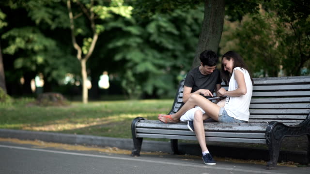 Two-girls-lesbians-use-tablet-on-bench-in-park