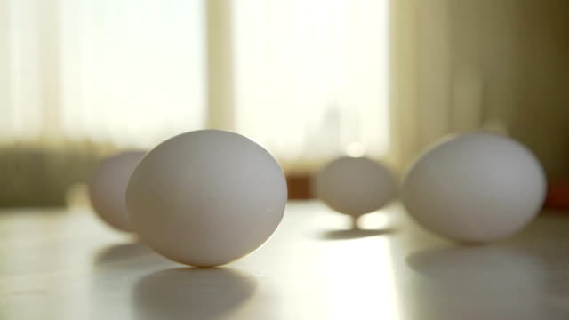 Cuatro-huevos-de-gallina-en-la-mesa-de-la-cocina-soleada,-un-huevo-se-gira