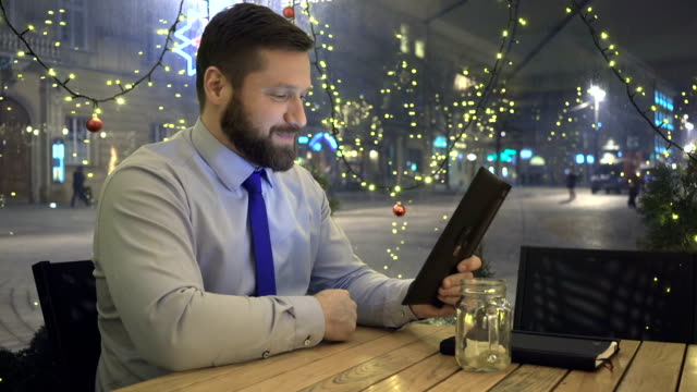 Businessman-has-video-call,-skype,-by-tablet-app-evening,-cafe,-christmas