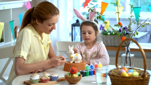 Frohe-Ostern!-Mutter-und-ihre-kleine-Tochter-mit-Hasenohren-malen-Osterhase