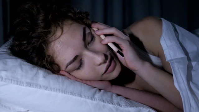 Close-Up-of-Female-Face-Talking-on-Mobile-Phone-in-Bed-at-Night