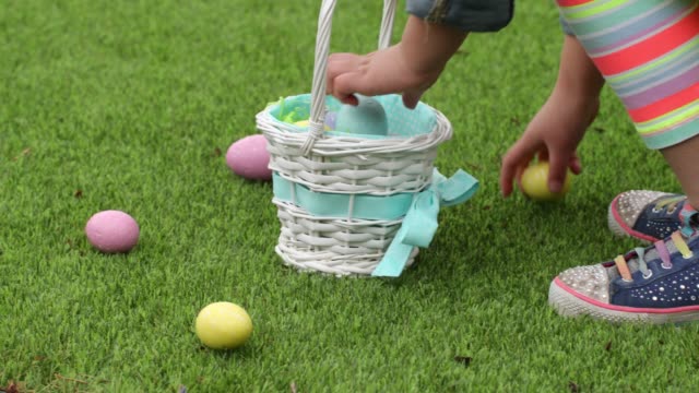 Young-girl-picking-up-Easter-eggs-in-grass-and-putting-them-into-basket