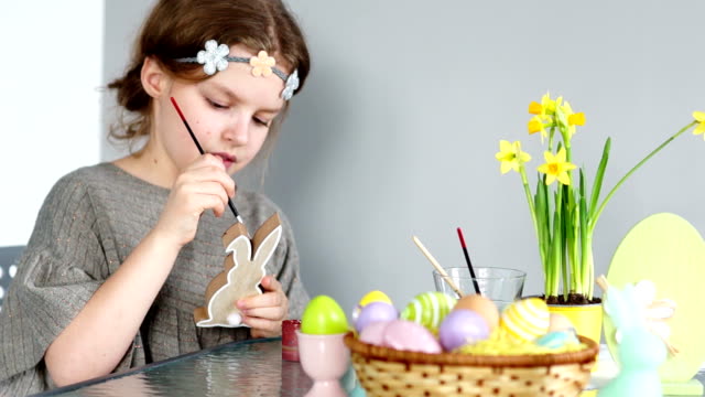 A-sweet-girl-prepares-for-Easter,-paints-the-Easter-bunny.-On-the-table-is-an-Easter-basket