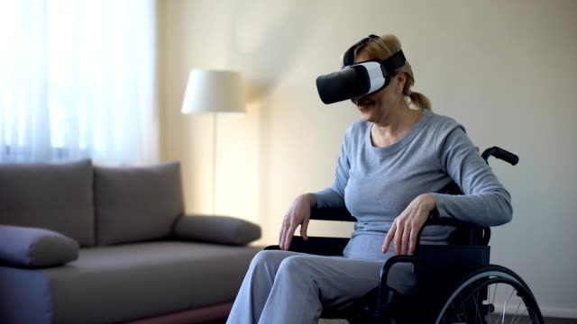 Retired-woman-in-wheelchair-wearing-vr-goggles-and-enjoying-game,-technology