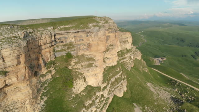 AÉREA:-Vuelo-sobre-un-acantilado-de-roca-alta,-revelando-una-vista-del-paso-en-Rusia-en-el-Cáucaso-Norte.-Fotografía-aérea-de-la-carretera-en-la-puesta-de-sol.-Vuelo-al-lado-de-la-roca