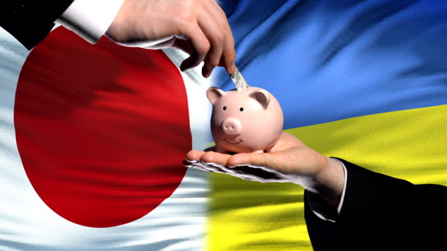 Japan-investment-in-Ukraine,-hand-putting-money-in-piggybank-on-flag-background