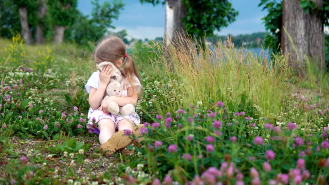 Ein-kleines-Mädchen-spielen-mit-einem-Spielzeug-Hasen-auf-der-Wiese-unter-den-blühenden-Klee