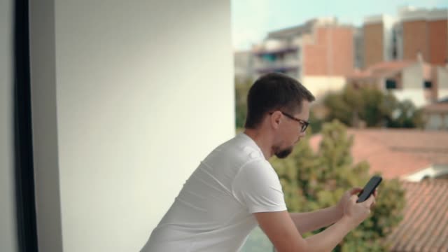 Männlichen-Benutzer-ist-Lesen-von-Nachrichten-im-Smartphone-Bildschirm-wischen,-stehend-auf-Balkon