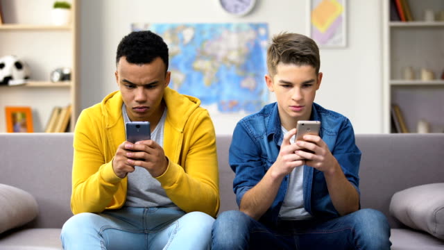Two-multiracial-teenagers-scrolling-smartphones-ignoring-each-other,-addiction