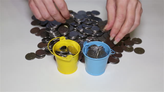 Girl's-hands-putting-coins-in-small-colorful-buckets