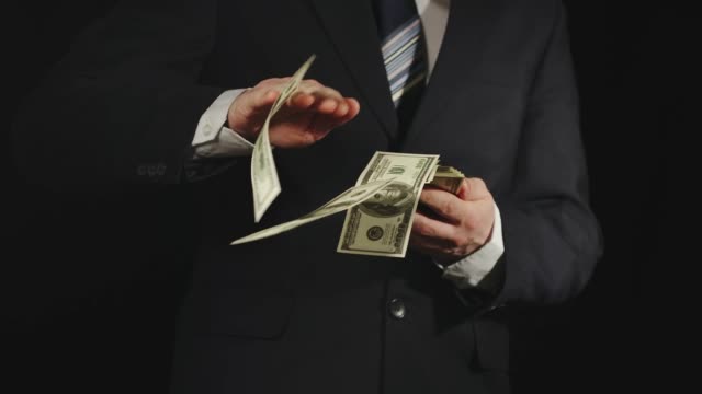 SLOW-MOTION:-Businessman-in-strict--suit-throws-bundle-of-US-dollar-bills-one-by-one---Front-View,