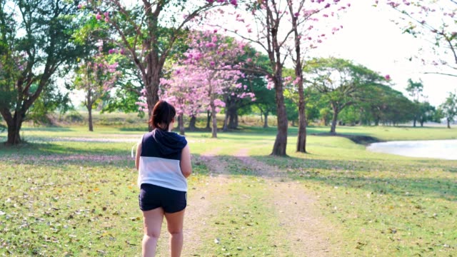Eine-dicke-asiatische-Frau,-die-morgens-im-natürlichen-Sonnenlicht-spazieren-geht.
Sie-versucht,-mit-Übung-Gewicht-zu-verlieren.--Konzept-Gesundheit-mit-Bewegung.-Zeitlupe